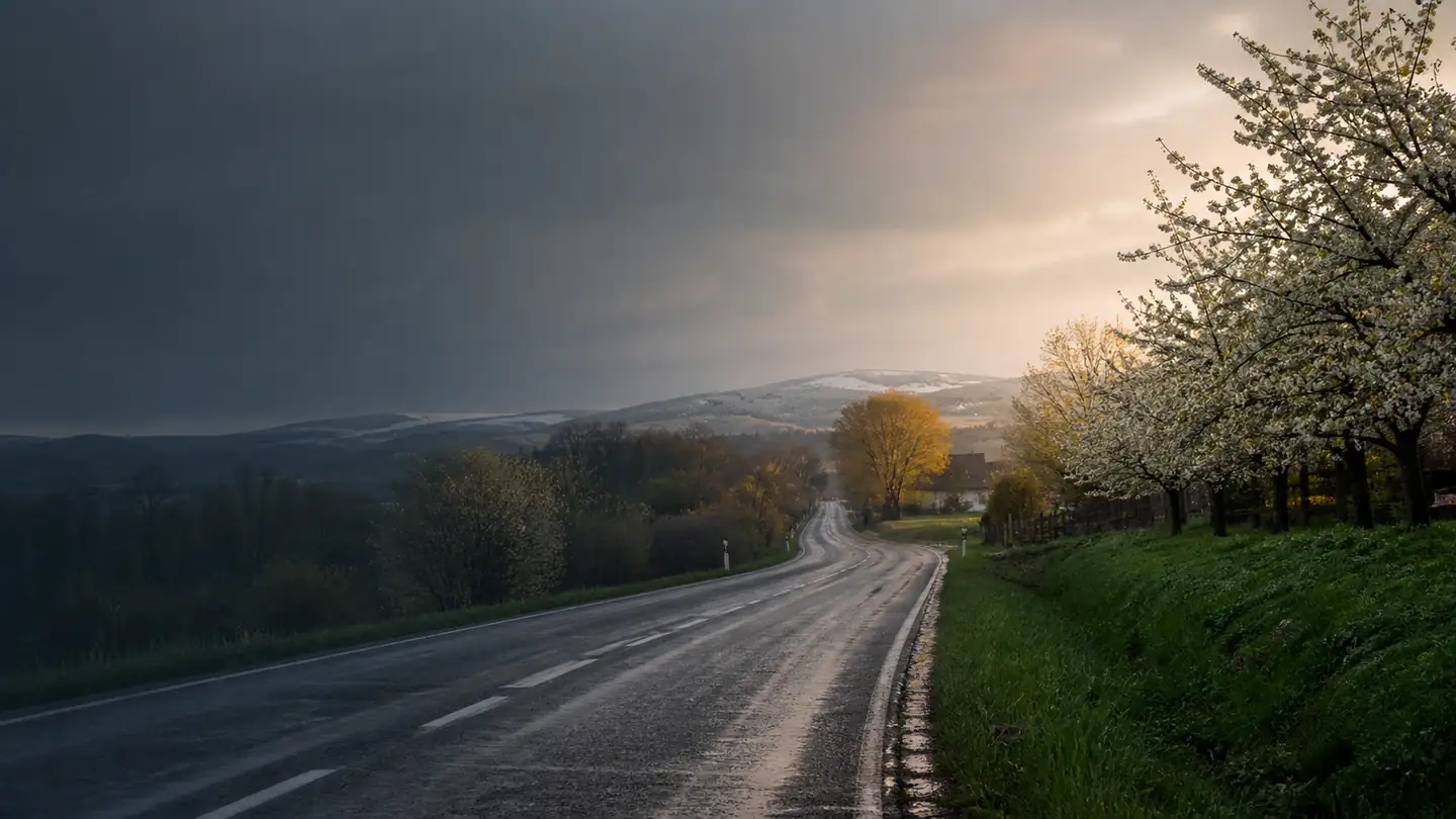 Pusta mokra droga obok kwitnącego sadu, jesiennych drzew i lekko ośnieżonych wzgórz - Crosswind Grip Peak 4S na deszcz, chłód i okazjonalny śnieg