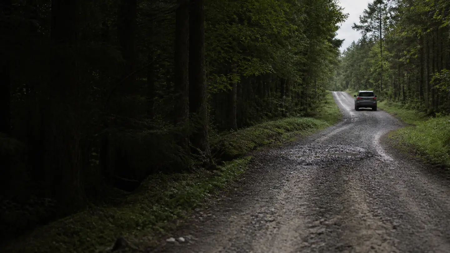 Niewielki samochód 4x4 oddalający się po mokrej leśnej drodze szutrowej - General Grabber AT3 między asfaltem a leśnym szutrem