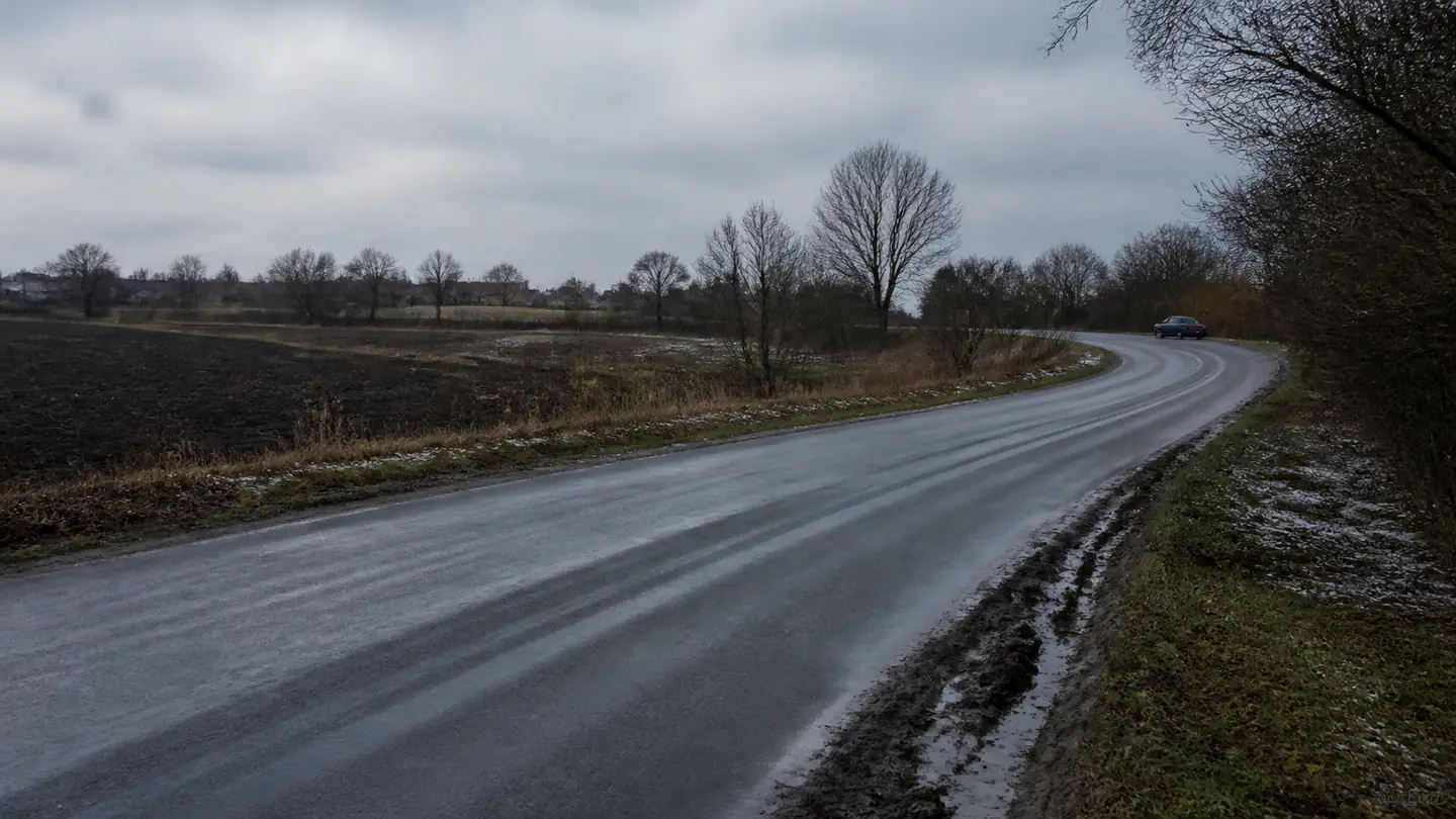 Małe auto w oddali na mokrej nizinnej drodze z resztkami topniejącego śniegu - Kormoran All Season na spokojne dojazdy przez cały rok