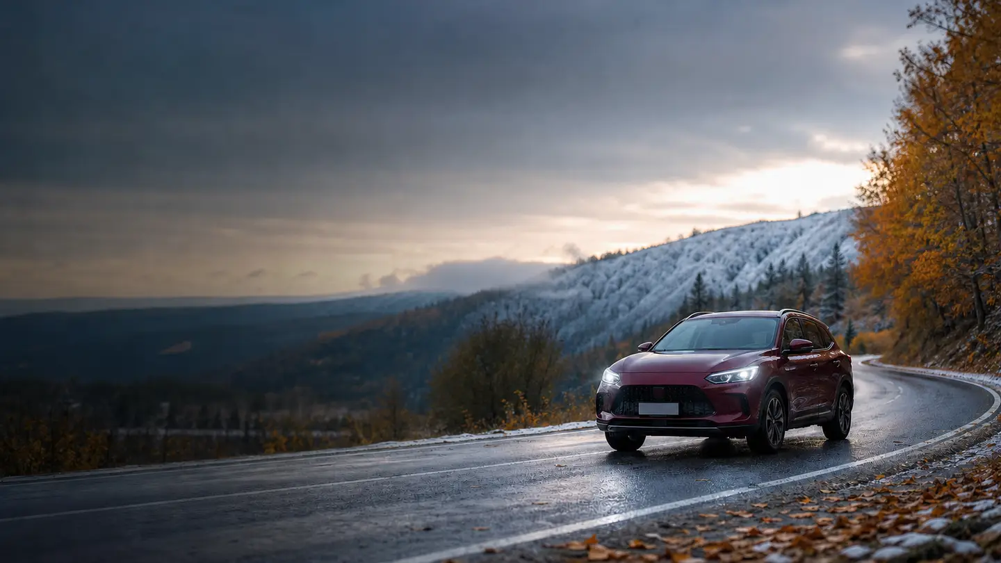 Bordowy crossover na mokrej drodze między jesiennym lasem i ośnieżonym wzgórzem - Kumho Solus 4S HA32 od jesiennego deszczu po pierwszy śnieg