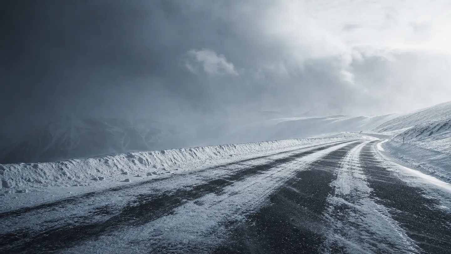 Pusta droga przez wysokie zimowe pustkowie z nawianym śniegiem i prześwitami asfaltu - RoadX RXFrost WU01 na mróz, śnieg i lód